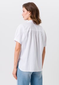 Witte blouse met korte mouwen en een rugpand met plooidetails, heeft een gebogen zoom en een relaxte pasvorm, gecombineerd met lichtblauwe denim jeans.