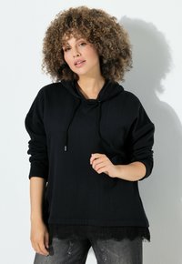 Černá mikina s kapucí a krajkovým lemem, s dlouhými rukávy a tkaničkou ve výstřihu. Modelka v uvolněné póze.