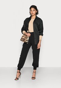 Svart skjorta med knappar, beige ribbad tröja, svarta tapered-byxor, svarta klackar med remmar och en handväska med zebraränder.