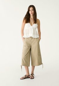 Top peplum bianco con dettagli in pizzo, abbinato a pantaloni cargo beige con tasche e lacci alle caviglie. Sandali neri con cinturini.