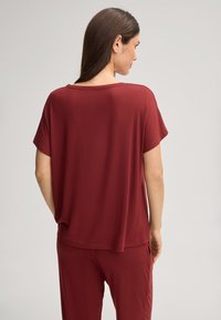Bordeaux kortemouwtop met een losse pasvorm, ronde halslijn en zachte textuur. De achterkant heeft een casual stijl en een drapeerontwerp.