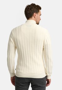 Cremefarbener, gestrickter Pullover mit vertikaler Rippenstruktur, hohem Kragen und enganliegenden Bündchen. Die lockere Passform betont den Tragekomfort.