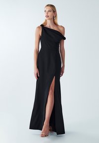 Czarna, asymetryczna suknia na jedno ramię z drapowanym stanikiem i rozcięciem do uda; gładka tkanina, długość do podłogi oraz minimalistyczny styl.