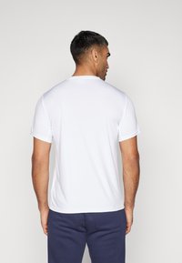 Camiseta atlética branca de mangas curtas com decote redondo, textura suave e um corte regular, apresentada de trás.