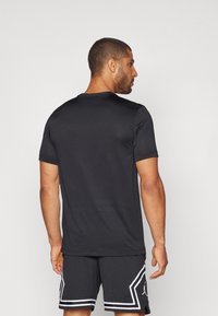 Svart kortermet treningsskjorte med rund hals. Glatt tekstur, tettsittende design, sammen med svarte shorts med hvite striper.