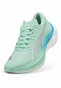 Zapatilla deportiva verde claro con parte superior de malla texturizada, cuello acolchado, diseño con cordones, acentos plateados y una suela azul acolchada.