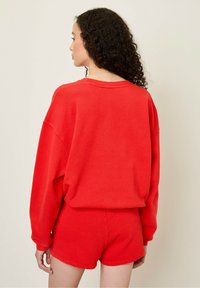 Röd sweatshirt och shorts set i mjukt material. Sweatshirten har en löst sittande passform och vida ärmar; shortsen är åtsittande med en enkel kant.