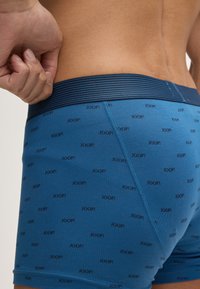 Siniset boxerit, joissa on musta toistuva "JOOP!"-logokuvio, raidallinen vyötärö ja sileä, hahmottava muotoilu.