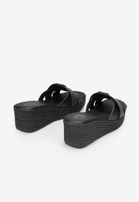 Sandalias de cuña negras con diseño de correas cruzadas, suela de textura trenzada y un ligero brillo en el material superior. Tacón elevado para mayor altura.