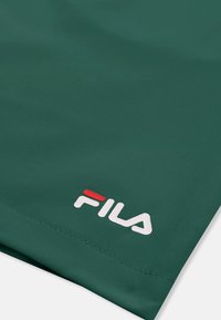 Tissu vert avec un ourlet cousu et un logo FILA blanc et rouge imprimé près du bord.