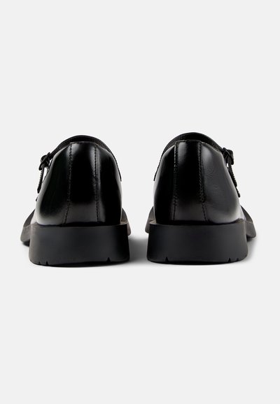 Scarpe in pelle nera con una finitura liscia, forma rotonda e suole in gomma basse; presentano una chiusura con lacci e dettagli di cucitura sulla tomaia.