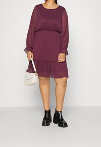 Sveske chiffon kjole med lange, samlede ærmer og en lagdelt nederdel, parret med sorte platform ankelstøvler og en cremefarvet håndtaske.