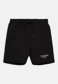 Pantaloni corti neri in cotone con vita elasticizzata e cordoncino, caratterizzati da un logo bianco "Calvin Klein Jeans" sulla gamba sinistra.