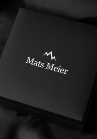 Zwarte cadeaudoos met een zilvergegraveerd logo waarop "Mats Meier" staat, met daarboven een minimalistische bergafbeelding.