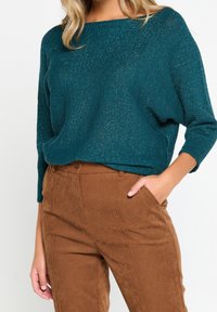 Tealtröja med lös passform och båtformad halsringning, med en strukturerad stickning med metalliska trådar. Matchas med karamelfärgade kordbyxor.