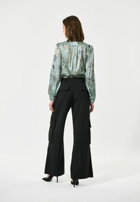 Top blouson floreale verde chiaro con maniche lunghe, abbinato a pantaloni cargo neri a vita alta con tasche laterali e gamba larga.