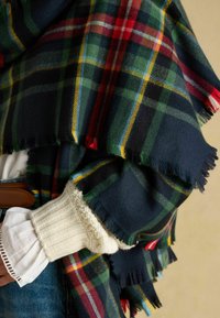 Tume ruuduline sall roheliste, punaste, siniste ja kollaste mustritega; ääred on narmendavad; koos tekstureeritud kreemja kampsuni varruka ja teksadega.