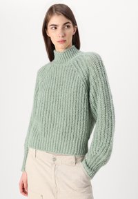 Minta zelena, debeo pleten cardigan z visokim ovratnikom, rebrasto teksturo in ohlapen kroj. Dolgi rokavi in nekoliko krajšan dolžina.