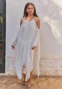 Robe longue et fluide de couleur blanche avec de fines bretelles et un décolleté bateau. Le tissu transparent présente des rayures subtiles, tombant en drapés jusqu'à un ourlet pointu.