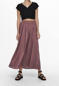 Schwarzes cropped Top mit V-Ausschnitt und kurzen Ärmeln, kombiniert mit einem fließenden, mauvefarbenen Maxirock mit elastischem Bund und Rüschendetails.