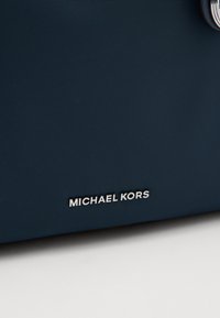 Borsa in nylon blu marina con superficie texture e dettaglio del logo argentato. Design semplice senza ulteriori motivi o accenti.