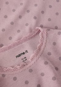 Roze stof met stippen en een geschulpte kantafwerking rond de halslijn, voorzien van gedrukte kledingmaatlabels EU 92 en US 2T.