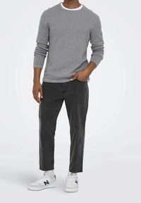 Harmaa teksturoitu neule, jossa on resorit hihansuissa, yhdistetty mustiin kapeneviin farkkuihin. Mallilla on valkoiset ja vihreät tennarit. Yksinkertainen ja rento ilme.