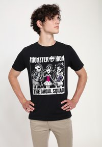 Zwart katoenen T-shirt met de afbeelding van "Monster High: The Ghoul Squad" met drie gestileerde personages in monochrome en gekleurde kleding.