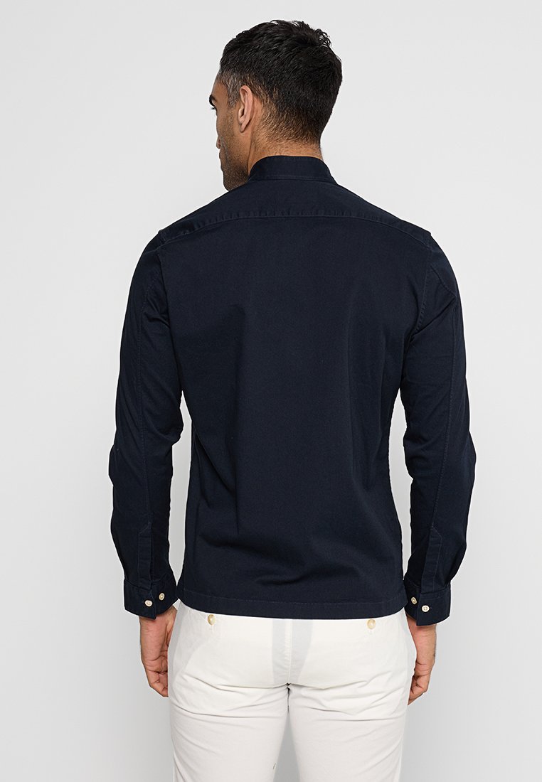 Marineblauwe katoenen overhemd met lange mouwen, een traditionele kraag, knoopmanchetten en een gladde textuur, van achteren bekeken.