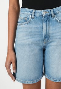 Shorts de mezclilla de talle alto en azul claro, con un diseño clásico de cinco bolsillos, costuras sutiles y un dobladillo enrollado en la parte inferior.