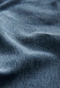 Gros plan sur un tissu en denim bleu montrant les détails de la texture et du tissage avec des plis doux et des ombres.