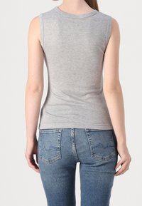 Top grigio senza maniche con scollatura rotonda, realizzato in morbido cotone, abbinato a jeans in denim blu con tasche posteriori e una leggera scoloritura.