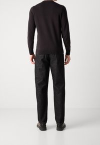 Pull en maille noir à manches longues, manches avec poignets côtelés et col rond, assorti à un pantalon texturé foncé et des chaussures noires.