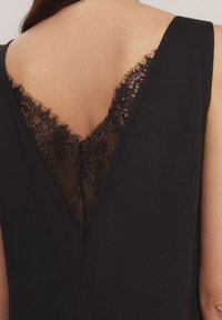 Vestido negro con un escote en V en la parte posterior y detalles de encaje. La tela suave, el diseño elegante y el intrincado ribete de encaje crean un contraste texturizado.