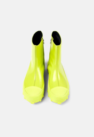 Neon yellow ankle boots with a glossy finish, featuring a ribbed rubber toe cap, side zipper closure, and textured soles.