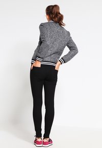 Grå struktureret bomberjakke med sort og hvid striped ærmer, parret med sorte skinny jeans og lyserøde sportssko, set bagfra.