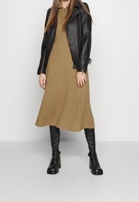 Sort lædermotorcykeljakke over en ribstrikket, knælængde, tanfarvet kjole. Høje sorte støvler med hæl fuldender outfittet. Enkel design med få detaljer.