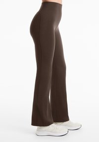 Leggings évasés marron avec une taille haute, fabriqués en matière extensible. Présentent des coutures visibles et une texture lisse et mate.