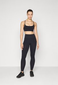 Sujetador deportivo negro y leggings de cintura alta de tela elástica, combinados con zapatillas atléticas negras. Diseño sencillo sin patrones visibles.