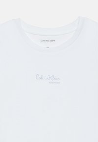 Λευκό βαμβακερό T-shirt με στρογγυλή λαιμόκοψη. Διαθέτει έναν φωτεινό μπλε εκτυπωμένο λογότυπο, "Calvin Klein," και "NEW YORK" από κάτω στην περιοχή του στήθους.