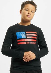Zwart shirt met lange mouwen met een grafisch ontwerp van een gestileerde Amerikaanse vlag in blauw en rood, met de tekst "NIET LOPEN, DANS!" eronder.