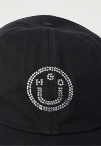 Schwarze Baseballkappe aus Stoff mit einem kreisförmigen Design aus kleinen silbernen Nieten, die ein Smiley-Gesicht mit Umlaut über dem Buchstaben U bilden.