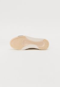 Hvid sneakersål med et struktureret tan gummigrebsbund. Har et stribet mønster på siden og branding ved buen.