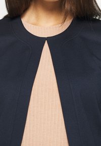 Námořnická modrá bunda s kulatým výstřihem a jemným prošíváním, zkombinována se světle růžovým ribkovaným topem.