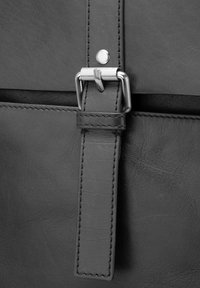 Detale czarnej skórzanej torby z metalowym zatrzaskiem, przeszywanym paskiem i gładką teksturą. Wyraźny srebrny element ozdobny.