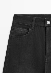 Schwarze Denim-Jeans mit geradem Schnitt, einer vorderen Tasche und einem Metallknopfverschluss an der Taille mit subtiler Textur.