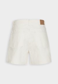 Shorts en denim blanc à coupe carrée, avec une surface texturée, deux poches arrière et une étiquette en cuir marron au niveau de la taille.