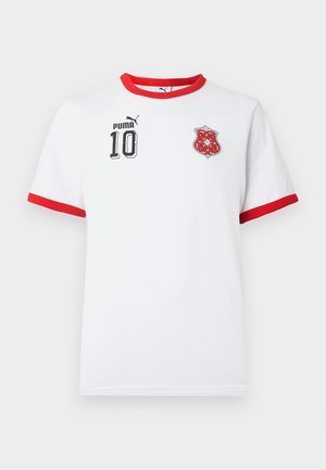 Bela športna majica Puma z rdečim ovratnikom in robovi rokavov, črno številko 10 in logotipom na levem prsnem delu ter rdečim keltskim emblemom na desnem prsnem delu.
