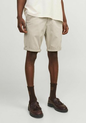 Beige shorts with a dotted pattern, rolled cuffs, paired with dark brown socks and shoes featuring a bow detail. Casual fit.