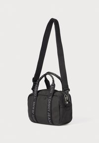 Zwarte nylon schoudertas met een ritssluiting, draaghandvatten en een gestreepte schouderband met de tekst "TOMMY JEANS". Compact, rechthoekig ontwerp.